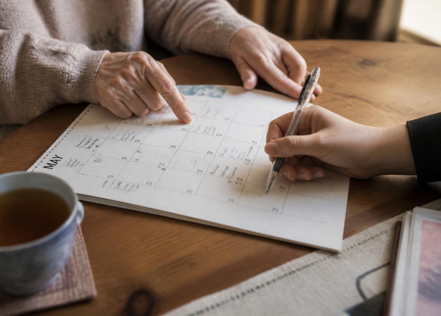 Two pairs of hands of different ages writing on a paper wall calendar